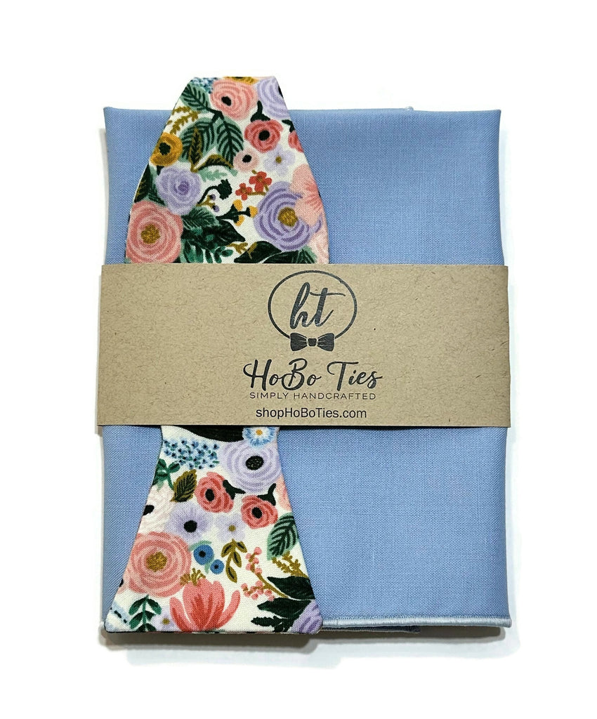 Ivory Garden Party Petite Floral Bow Tie with floral pattern on a blue background, handcrafted neckties for men.